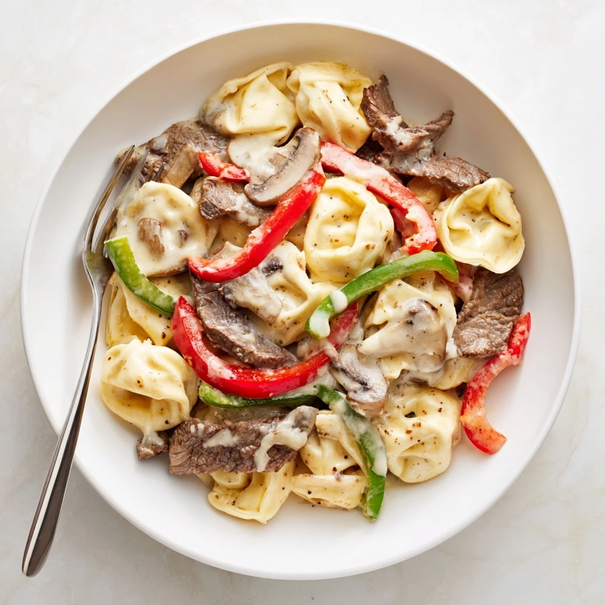 Slow cooker cheesesteak tortellini featuring seared steak slices, mushrooms, and rich cream sauce