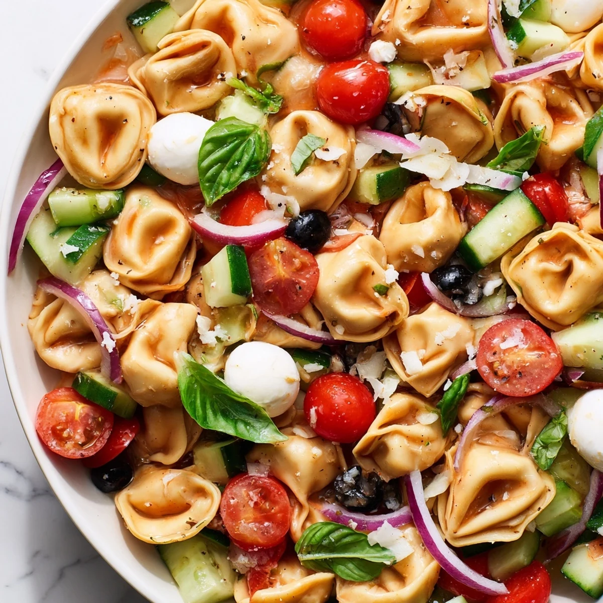 Tortellini salad in a bowl featuring crisp vegetables, fresh basil, and Parmesan cheese