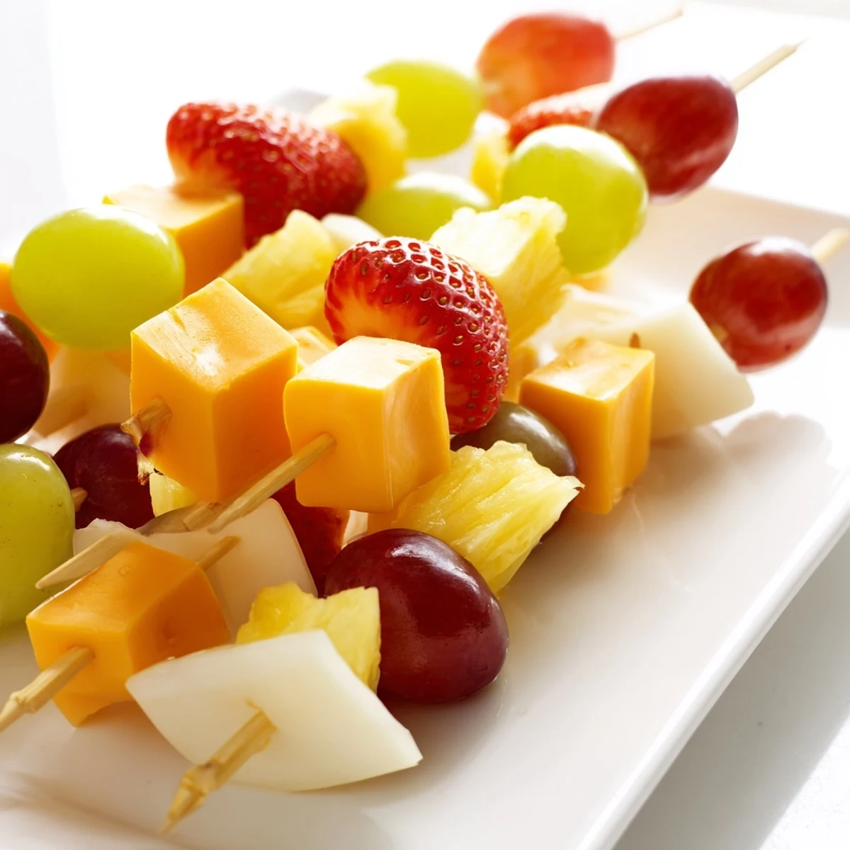 Colorful fruit and cheese kabobs arranged on a white platter with fresh mint garnish