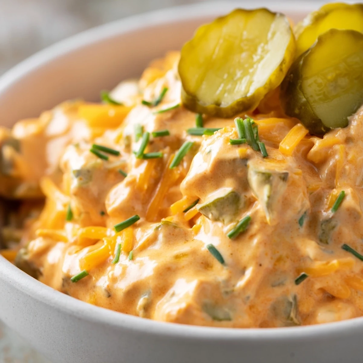 Tangy buffalo pickle dip topped with cheddar cheese and fresh chives in a rustic bowl