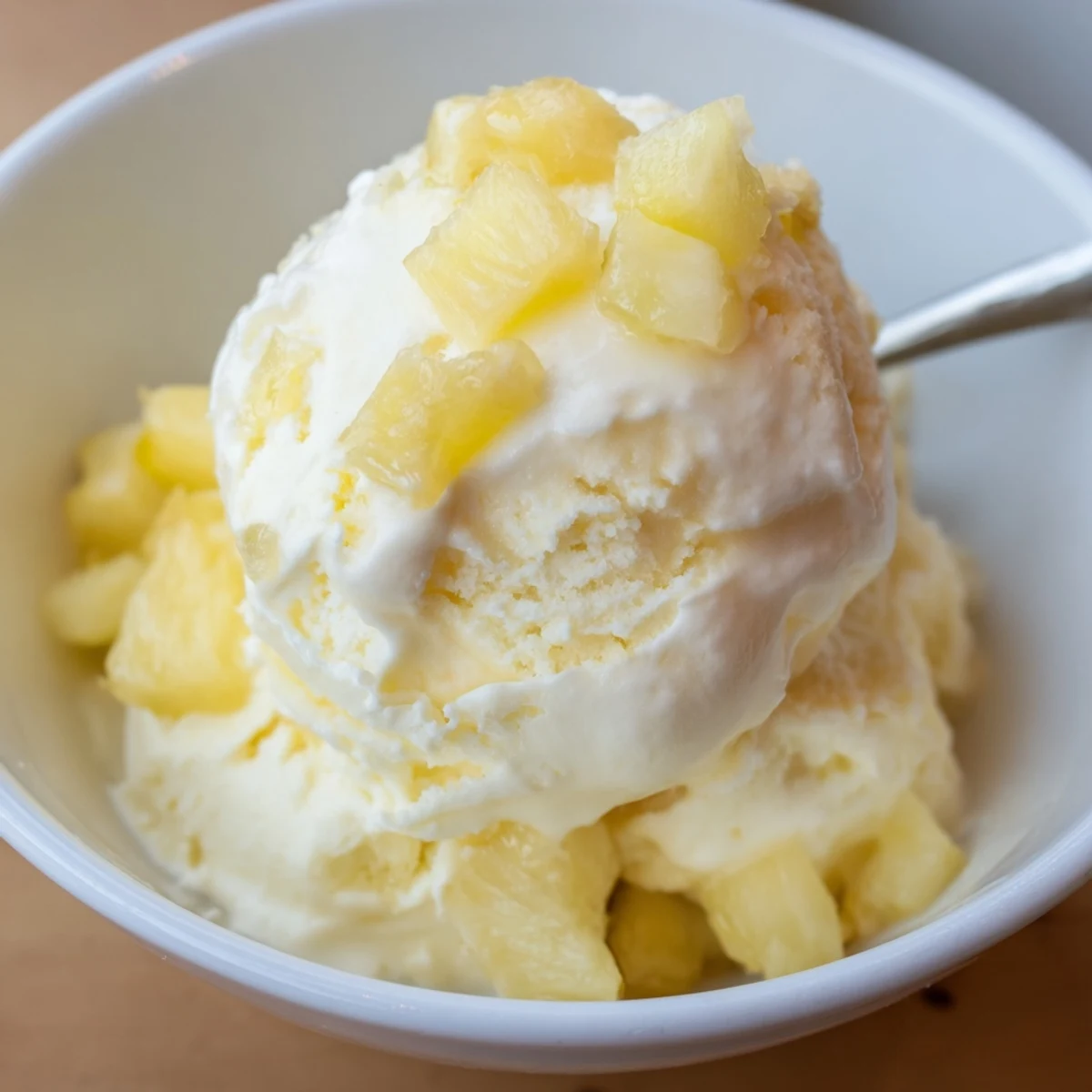Creamy Pineapple Ice Cream scoops melting slightly on plate, tropical aroma.