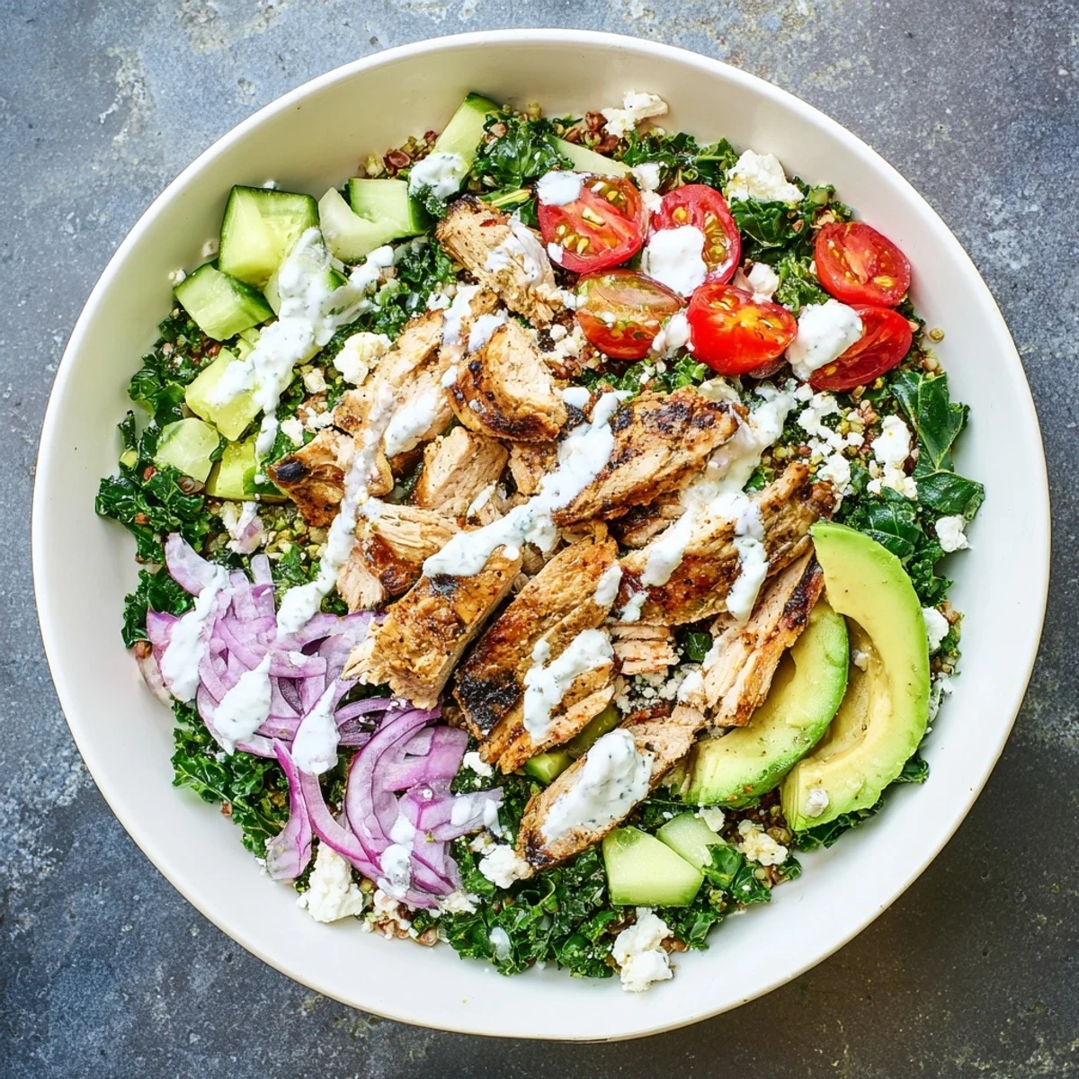 Colorful marinated kale and chicken bowls topped with fresh vegetables and zesty yogurt dressing in a white serving bowl